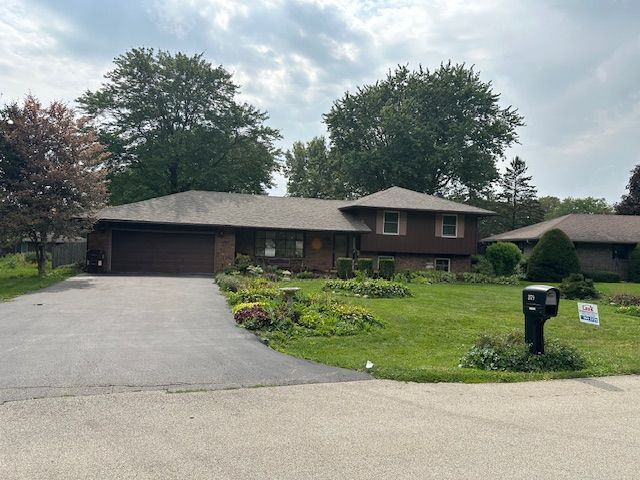 Suburban brick house with attached garage, driveway, front lawn, and two mailboxes under cloudy sky