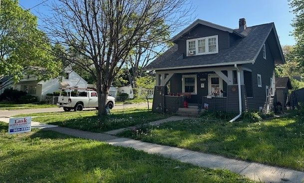 Blue house with a front porch and yard, a parked white truck, and a real estate sign by the sidewalk.