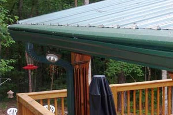 Deck with green roof edge, wooden railing, hanging red feeder, and closed black patio umbrella in a wooded yard