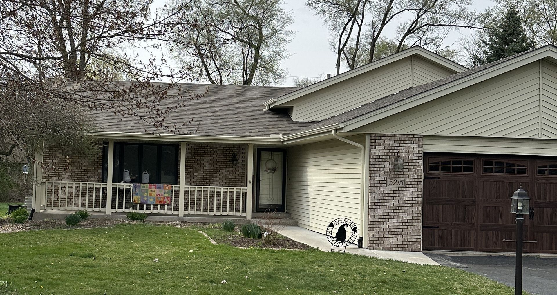 Suburban house with front porch, attached garage, and trees in the yard