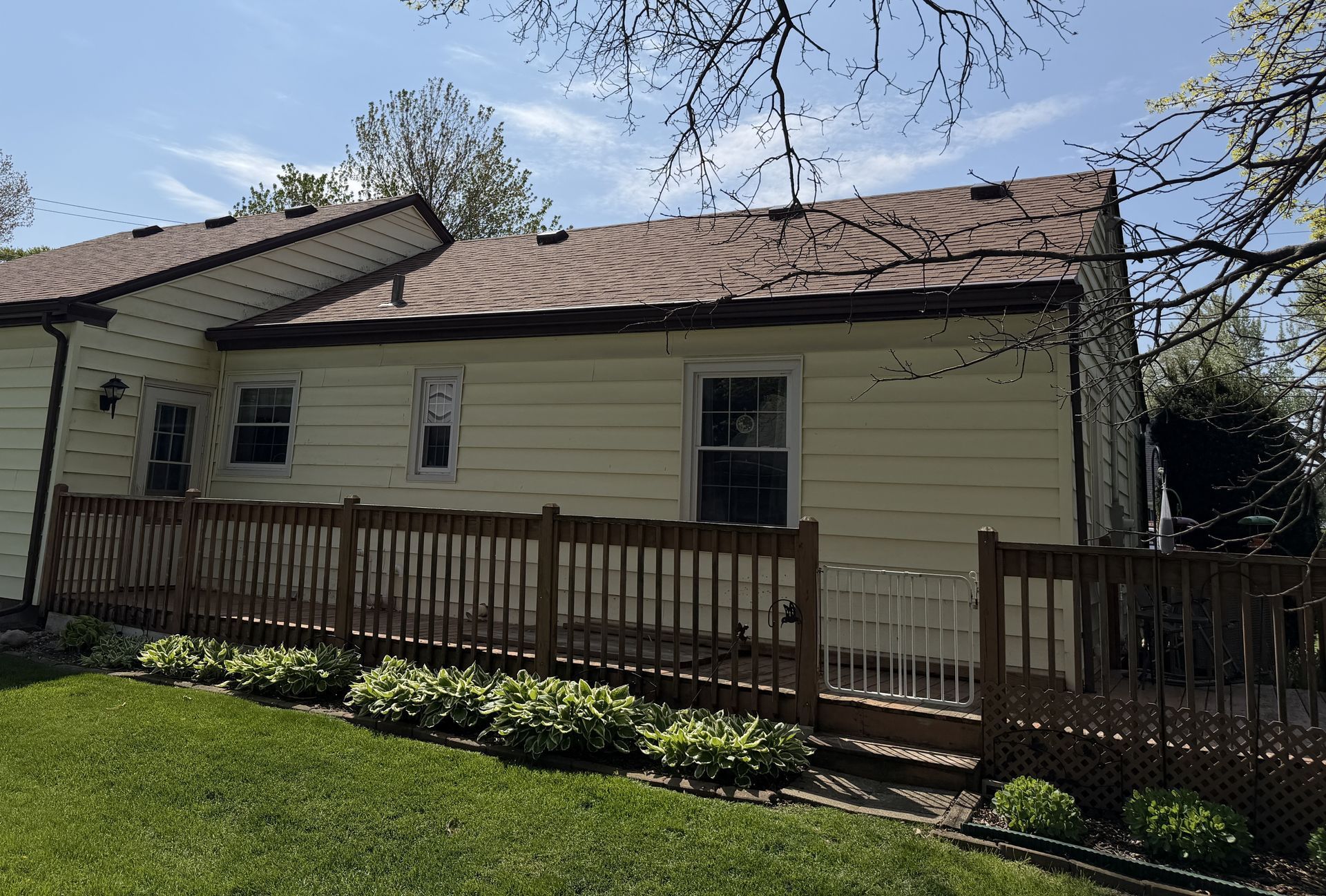 Single-story beige house with a wooden porch railing and green lawn under a blue sky