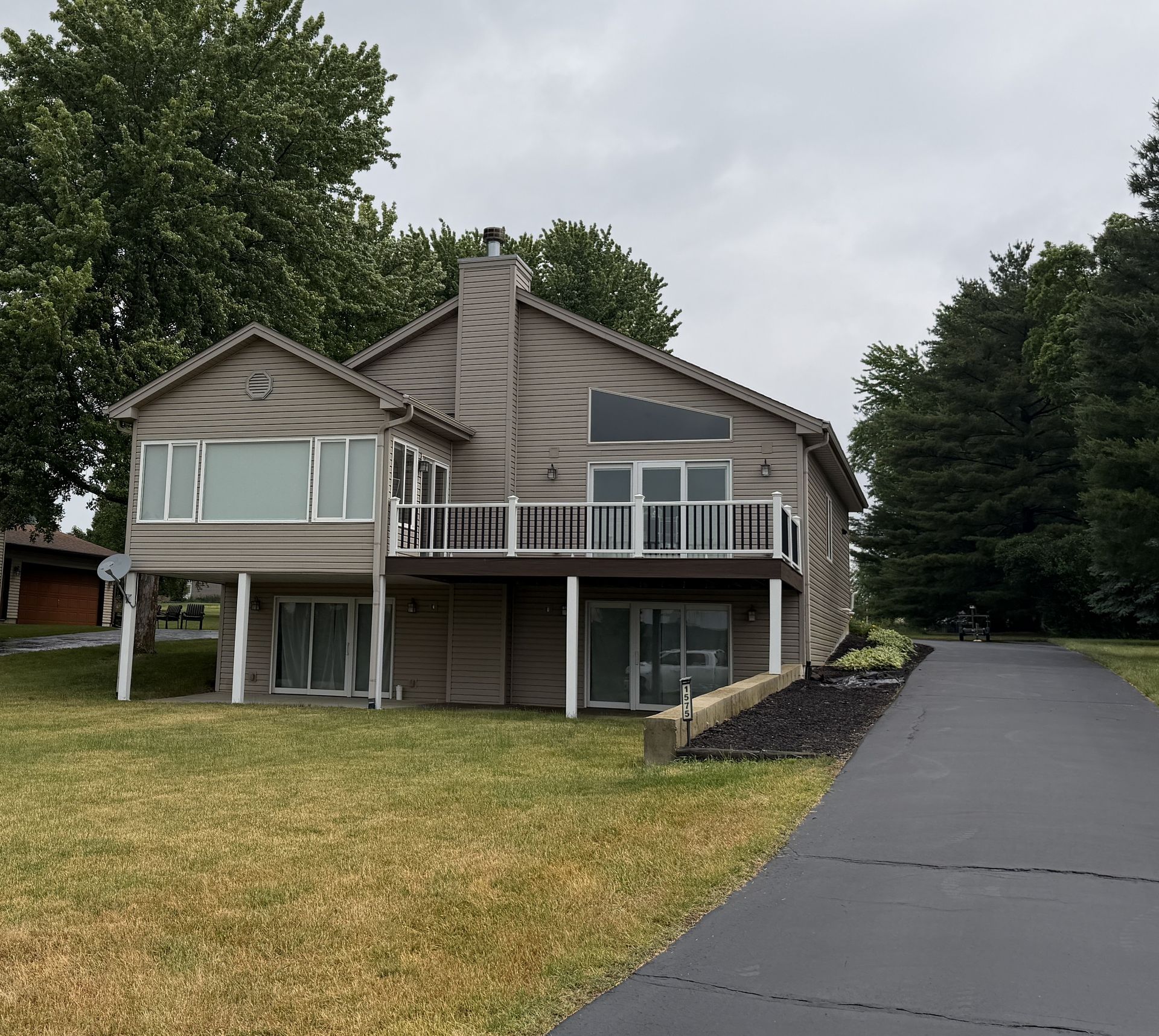 Suburban house with balconies and a paved driveway beside a lawn and trees