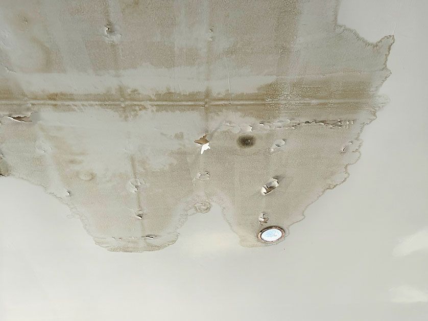 Water-damaged ceiling with peeling paint, stains, and exposed repair patches