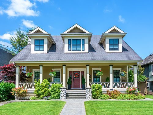 Charming white house with a front porch, green lawn, and three dormer windows under a blue sky