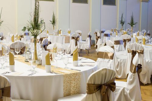 Elegant outdoor banquet tables set with white linens, gold accents, and floral centerpieces in bright sunlight