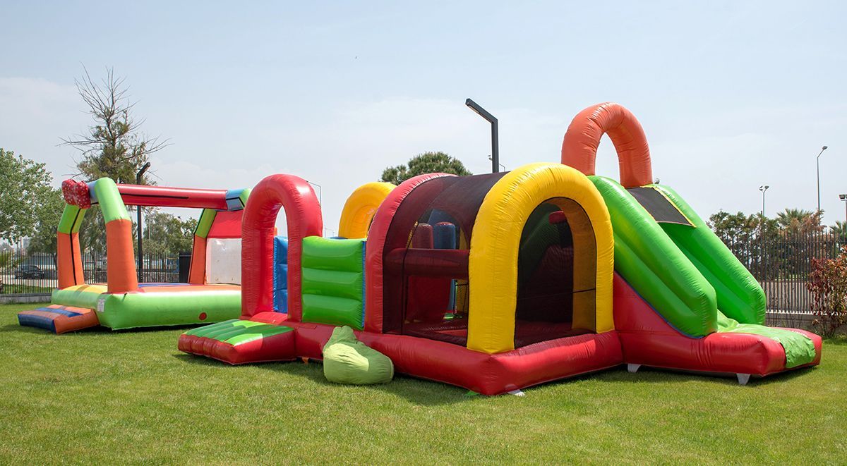 Colorful inflatable obstacle course on grass, with red, green, yellow, and orange slides and tunnels.