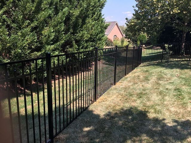 Black metal fence in a yard with green grass and trees, and a house in the background.