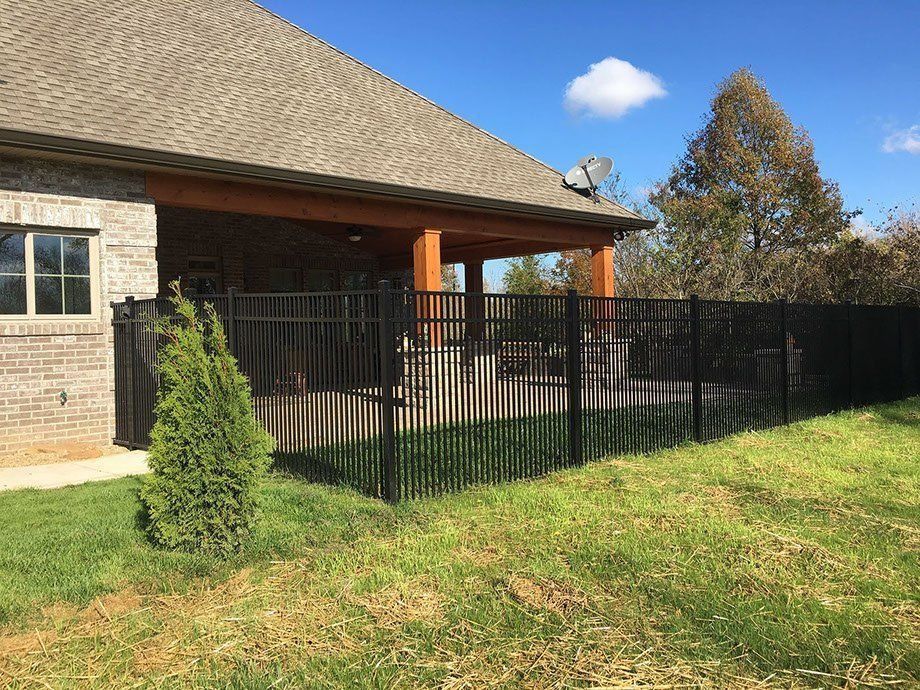 Black metal fence surrounding a patio next to a brick house. Green grass and blue sky.
