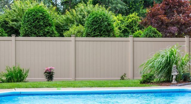 Tan privacy fence behind a blue swimming pool, lush green and red foliage in the background.