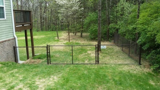 Black chain-link fence encloses a backyard with a deck. Green grass and trees are in the background.
