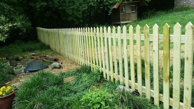 Wooden picket fence curving along a grassy yard with a small building in the background.