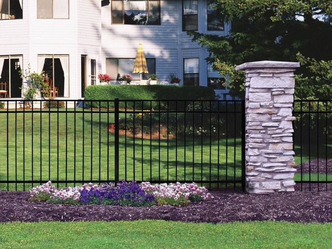 Black metal fence with stone pillar and purple flowers in front of a house.