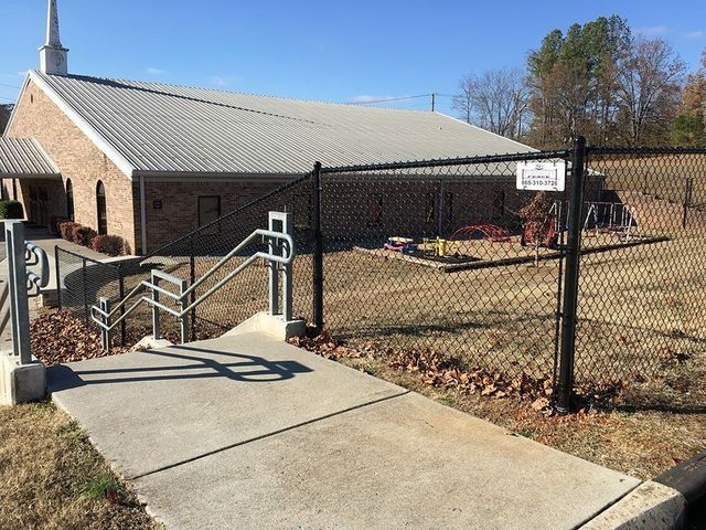 Concrete pathway with metal handrails leading to a church behind a black chain-link fence.