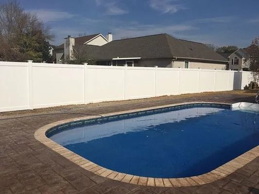 White vinyl fence around a blue swimming pool in a residential backyard on a sunny day.