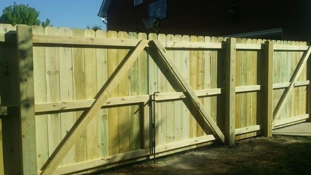 Wooden fence with gate, light green color, supporting beams, in an outdoor setting.