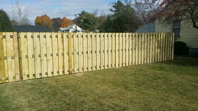 Wooden fence in a grassy yard, beside a house with autumn foliage in the background.