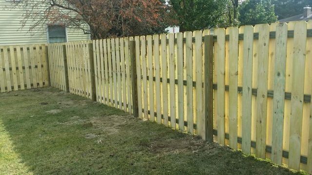 Wooden fence in a backyard, with green grass and a house in the background.