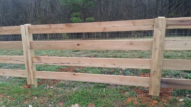 Wooden fence with horizontal boards, wire mesh, and vertical posts in a grassy area.