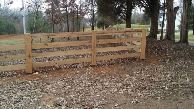 Wooden fence in a yard with fallen leaves and trees in the background.