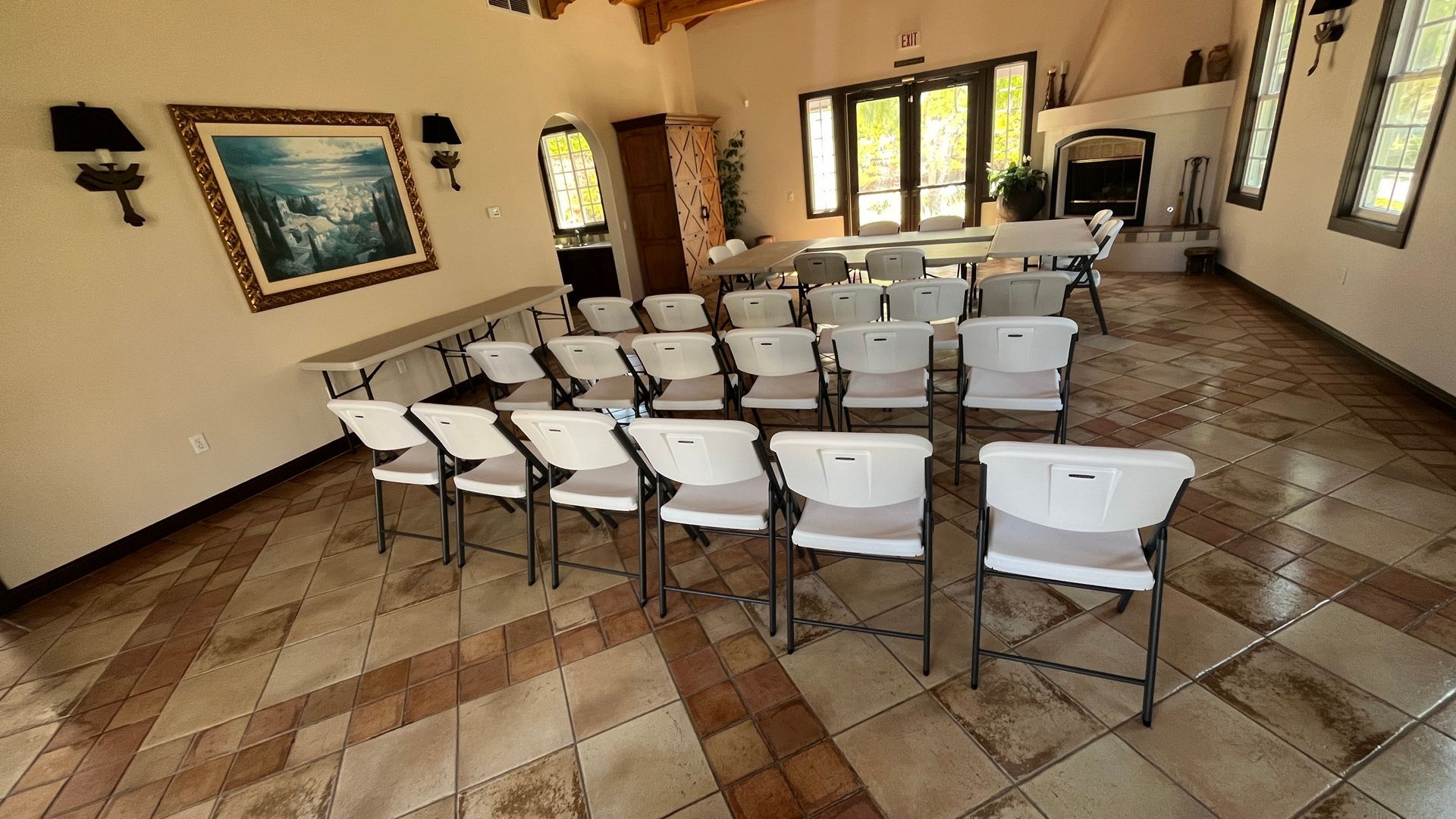 Rows of white chairs arranged in a hall with tiled floors and windows.