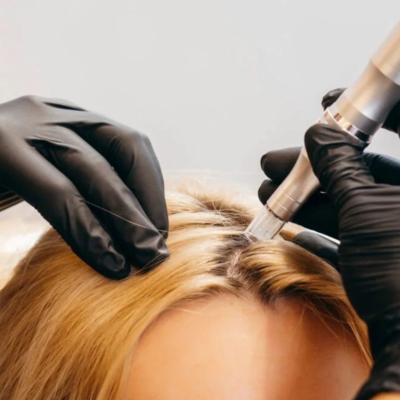 A woman is getting her hair done by a person wearing black gloves