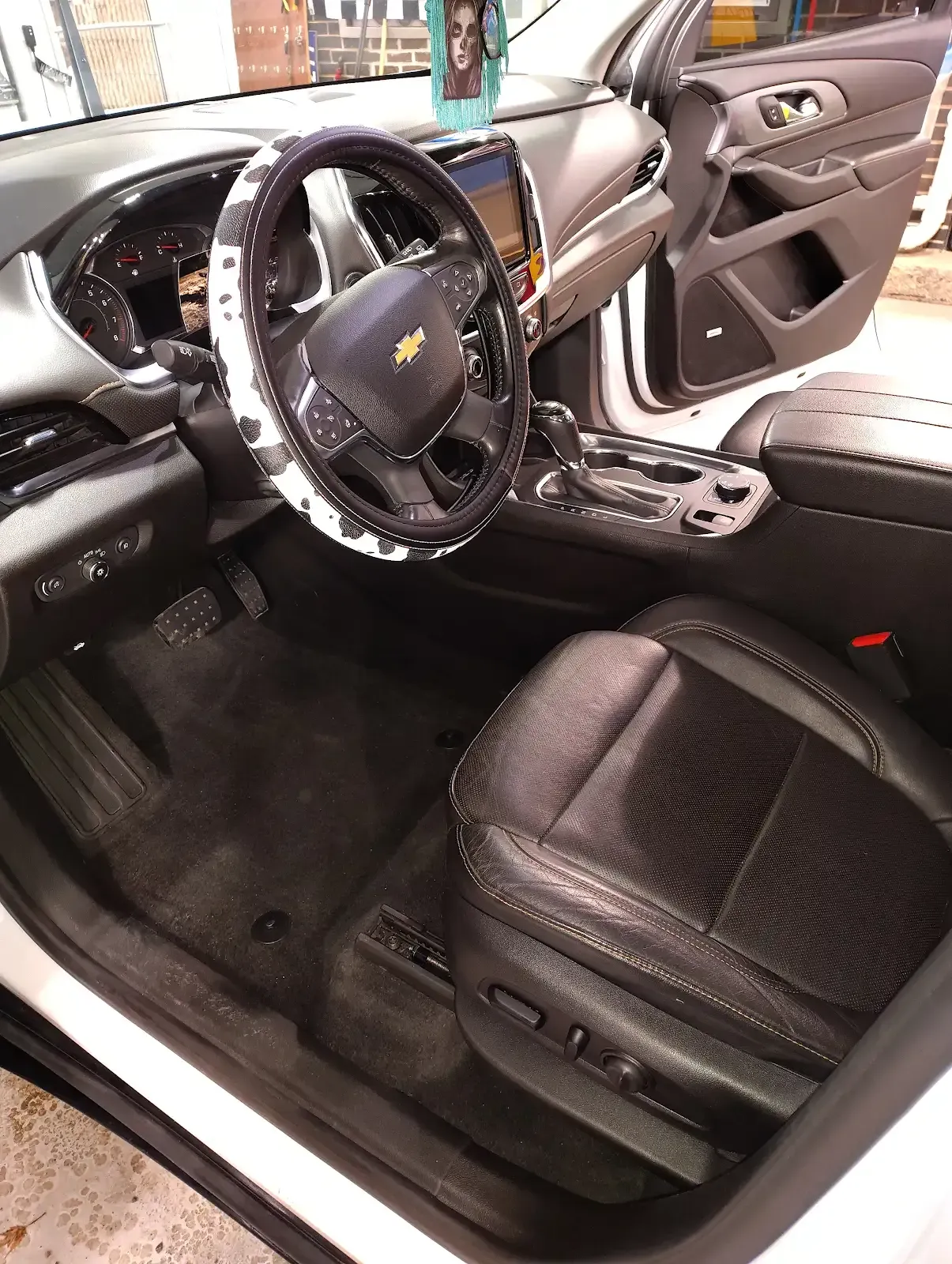 The interior of a Chevrolet vehicle featuring a black leather driver's seat and a black-and-white patterned steering wheel.