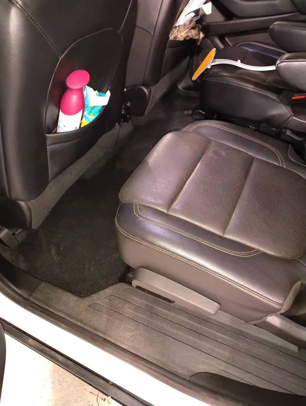 Back seat of a car showing black leather upholstery, a seat-back storage pocket, and a clean floor mat.