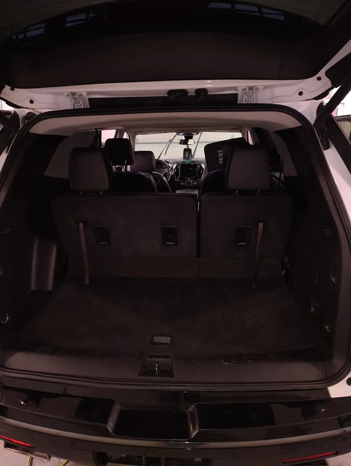 View from the open tailgate into the dark-toned interior of a white SUV, showing the cargo area and rear seats.