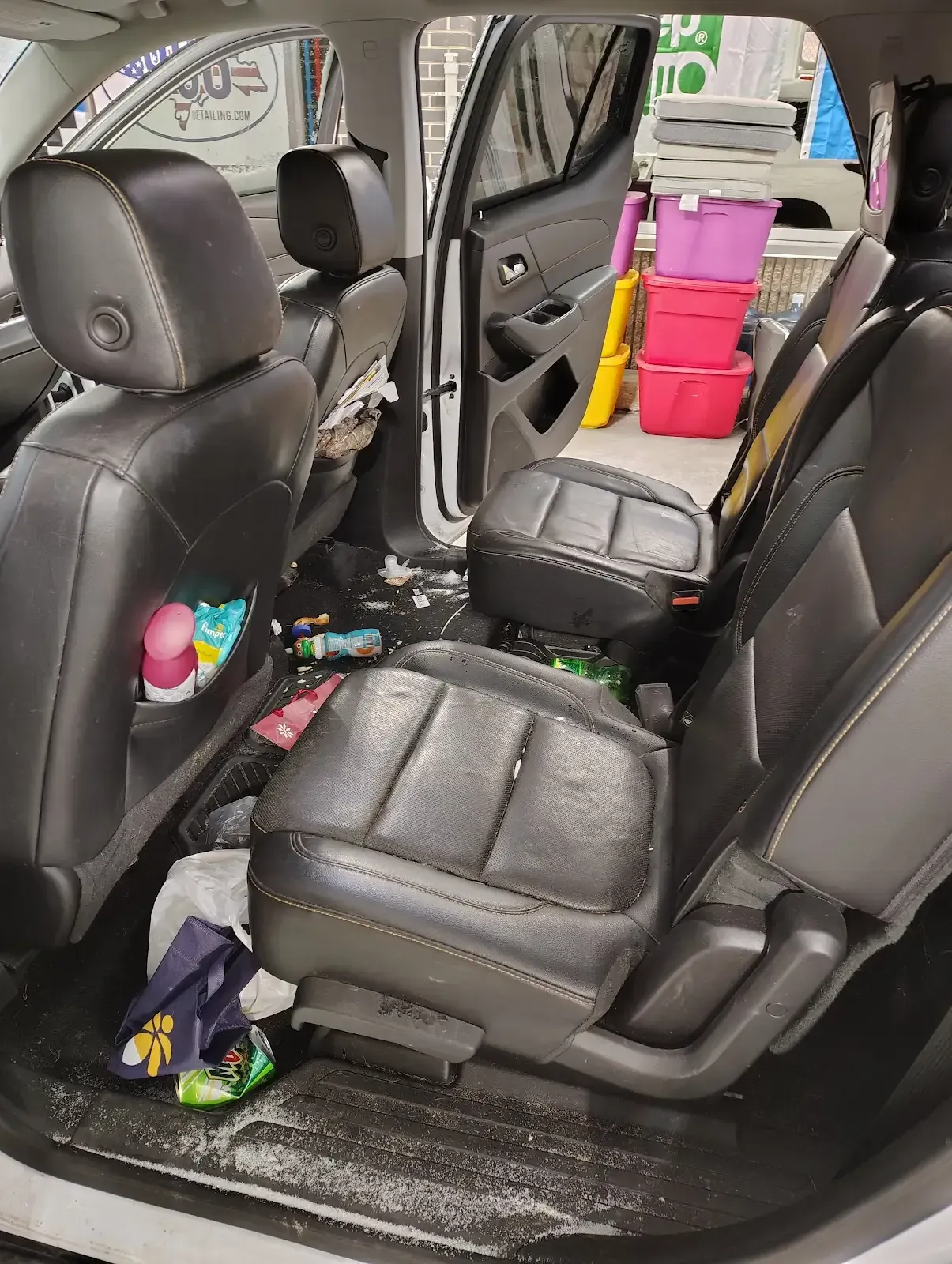 The back seats of a car are messy, with debris on the floor and stacked colorful storage bins visible through the door.