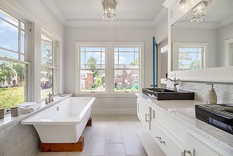 A bathroom with a tub, sink, mirror, and two windows.