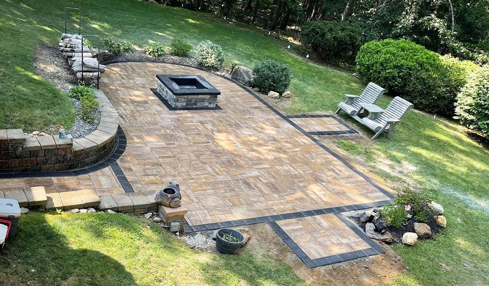 Backyard patio with fire pit, pavers, and seating surrounded by green grass and landscaping