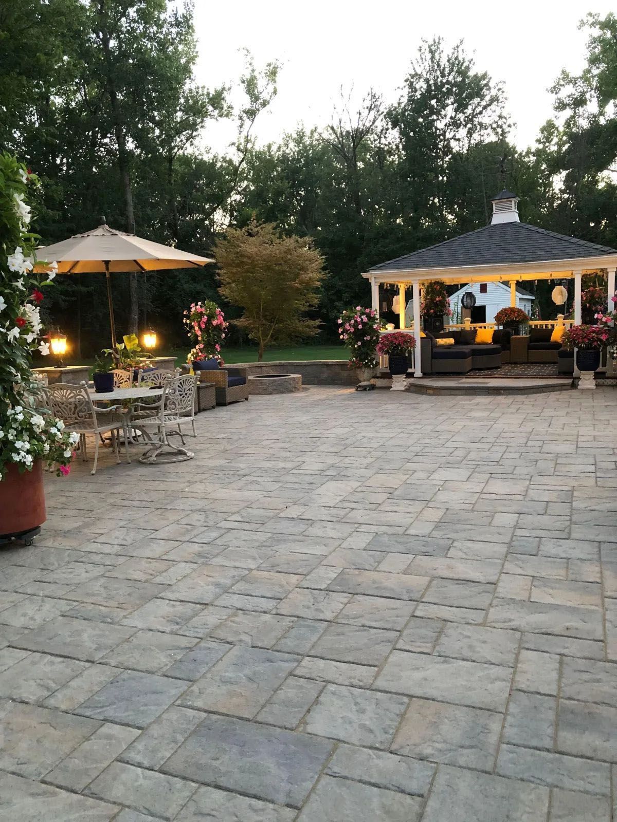 Stone patio with gazebo, umbrella, and flower pots; trees in background
