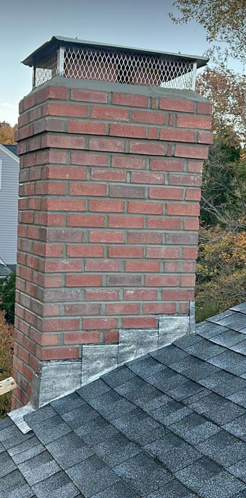 Brick chimney with metal cap, on a roof with gray shingles