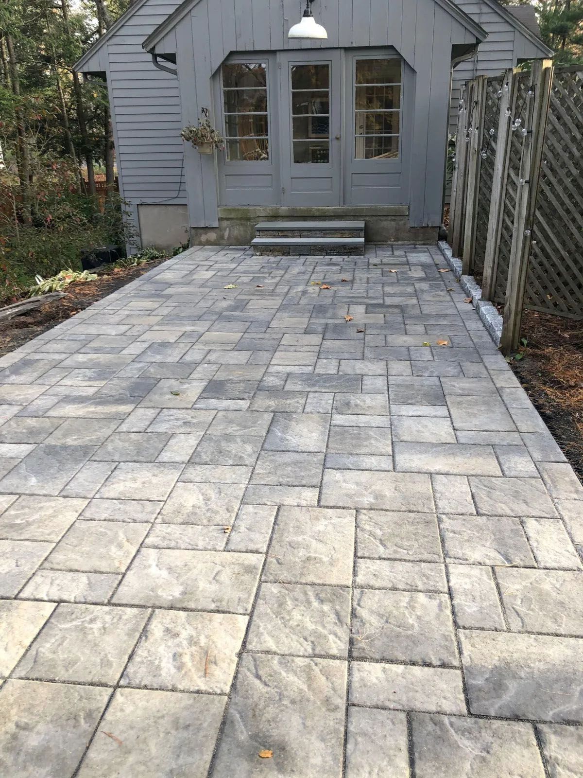 Gray stone pavers lead to a gray shed with double doors and a small stoop