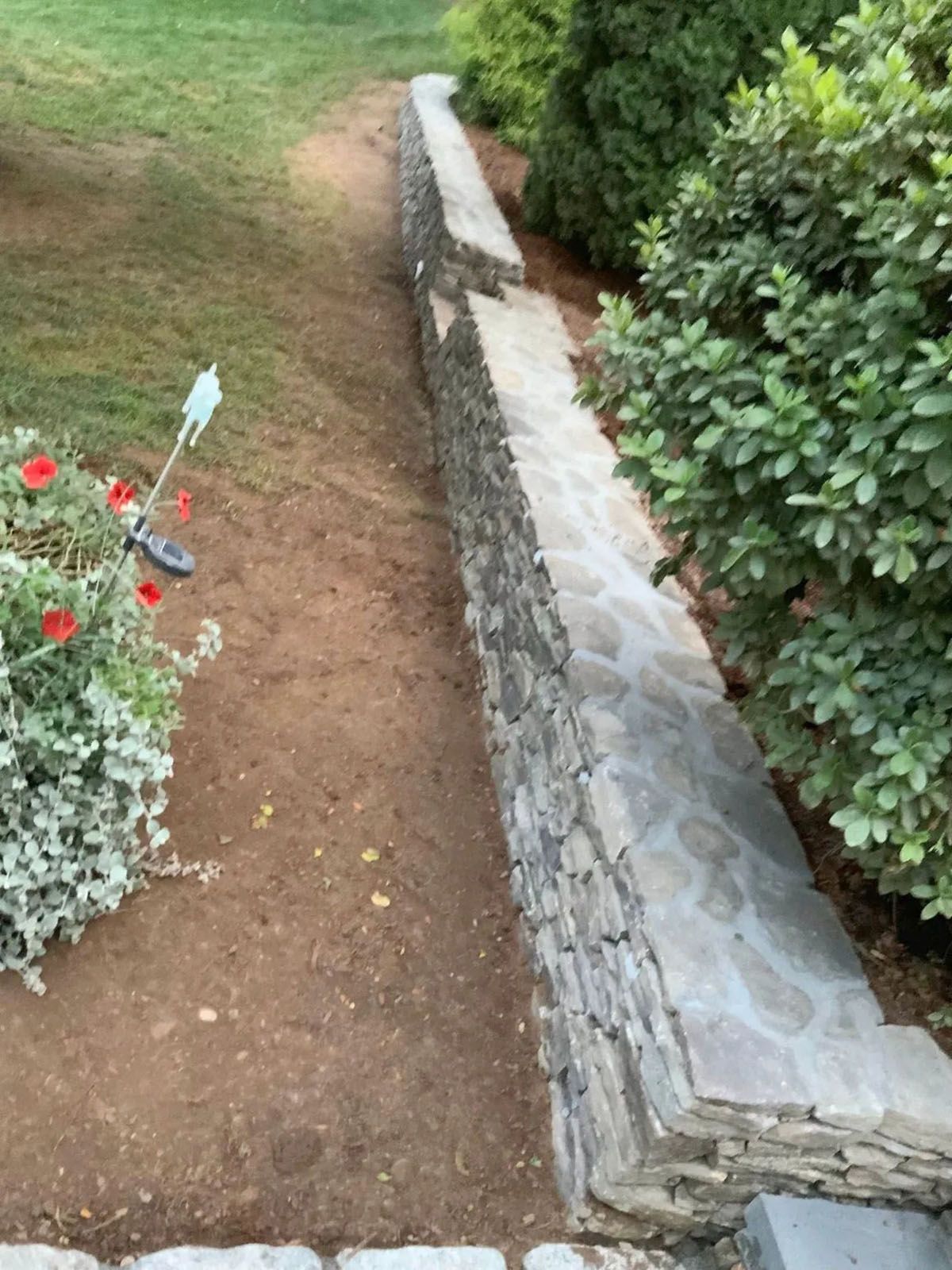 Stone wall with a pathway alongside a green lawn and bushes