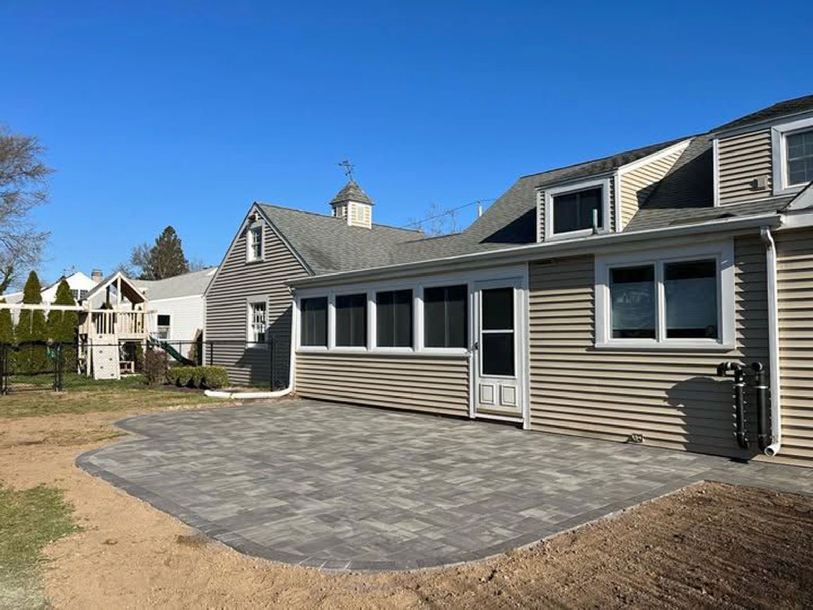 Backyard patio with gray pavers, beige house siding, and blue sky