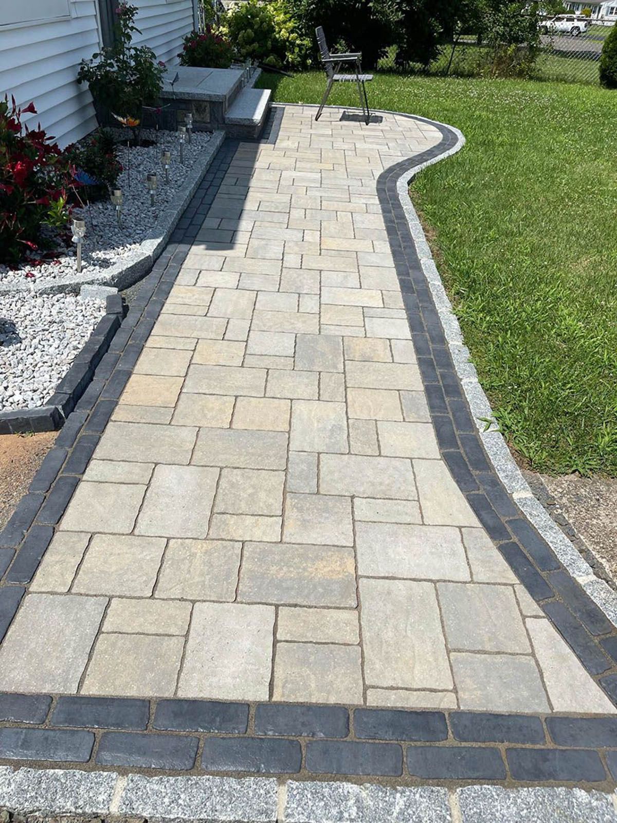 Stone walkway leading to a house, bordered by dark gray bricks and granite