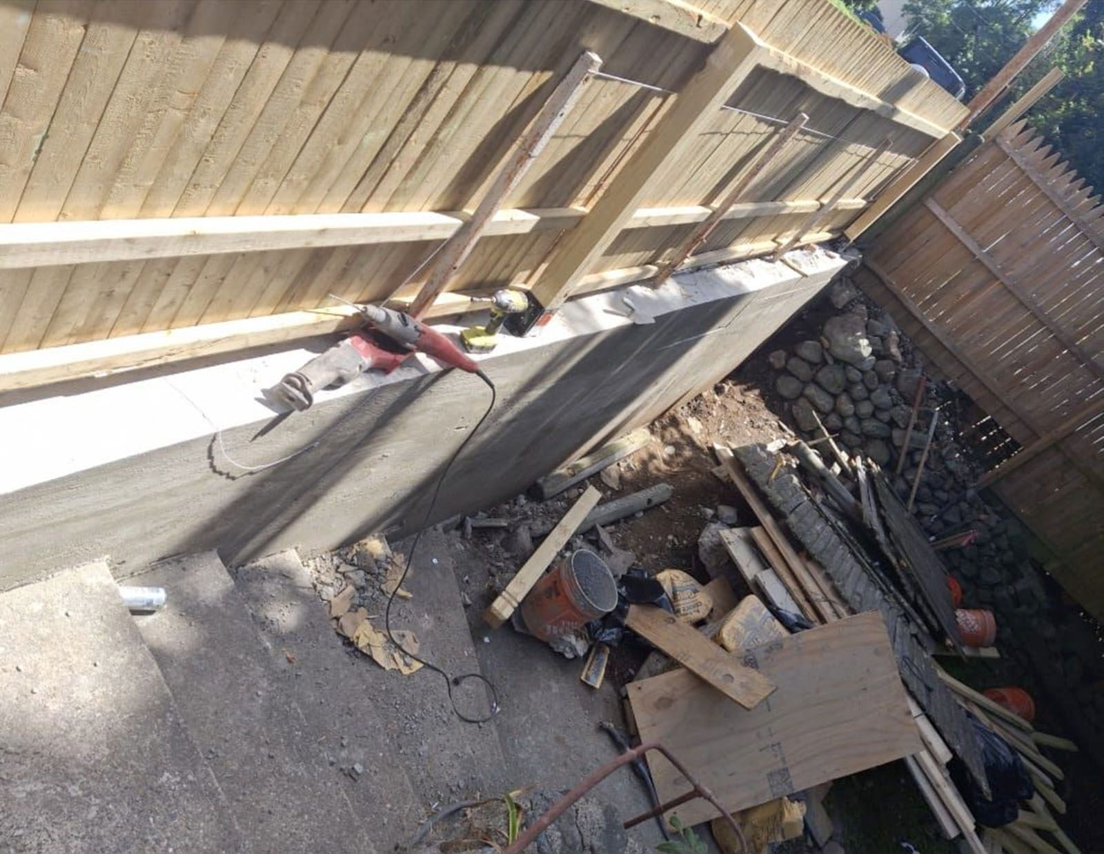 Construction site with a concrete wall, wooden fence, tools, and debris