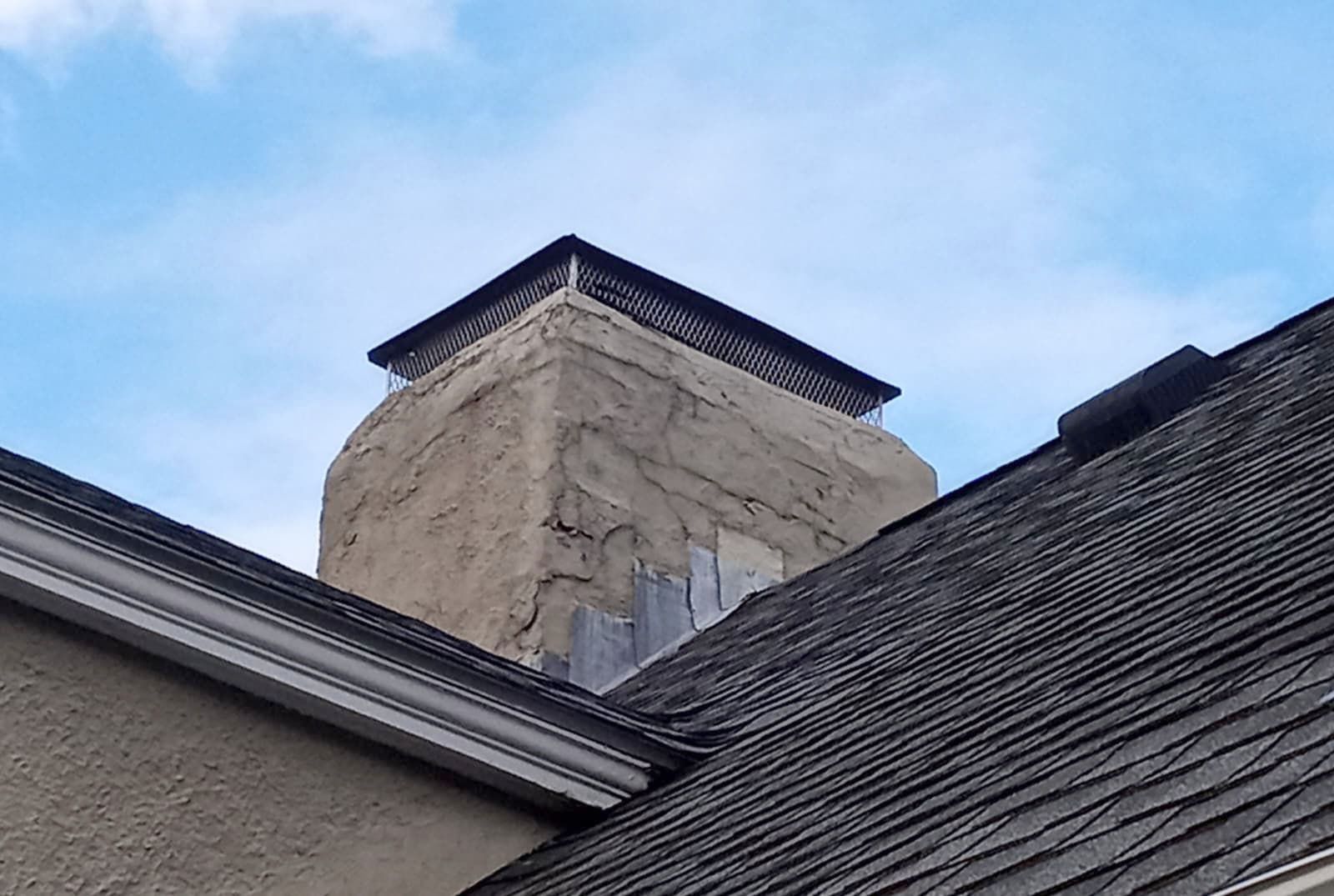Chimney on a house with a protective cover against a blue sky.