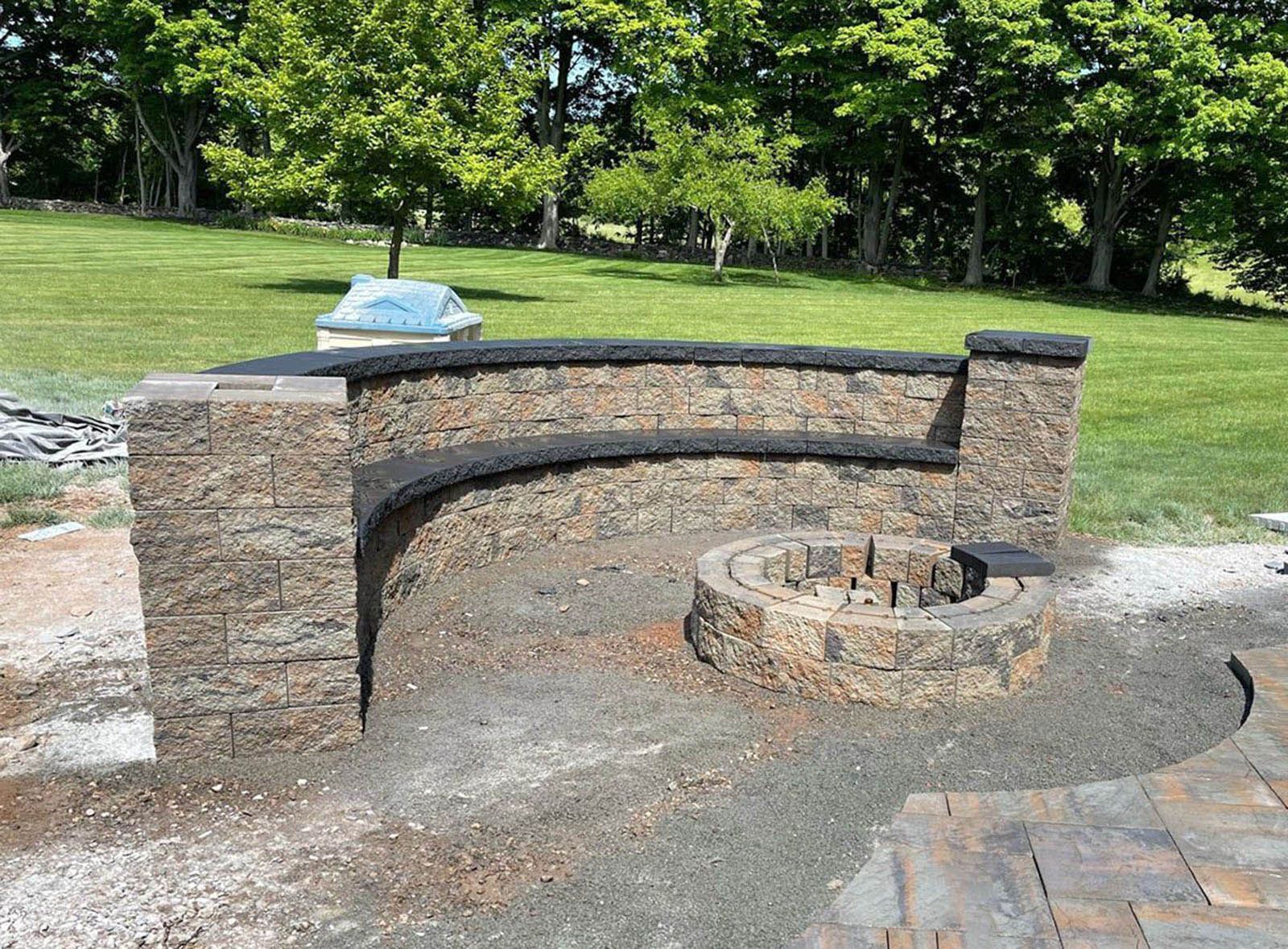 Stone seating and fire pit on a patio, surrounded by grass and trees