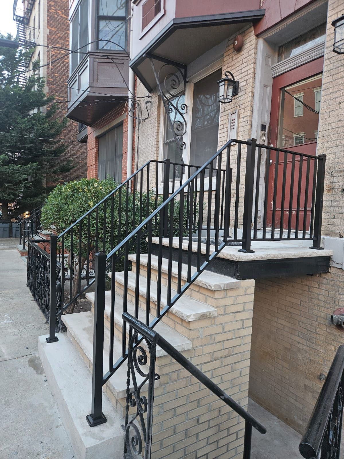 Exterior view of brick building with stairs, black iron railings, and a small awning over the front door