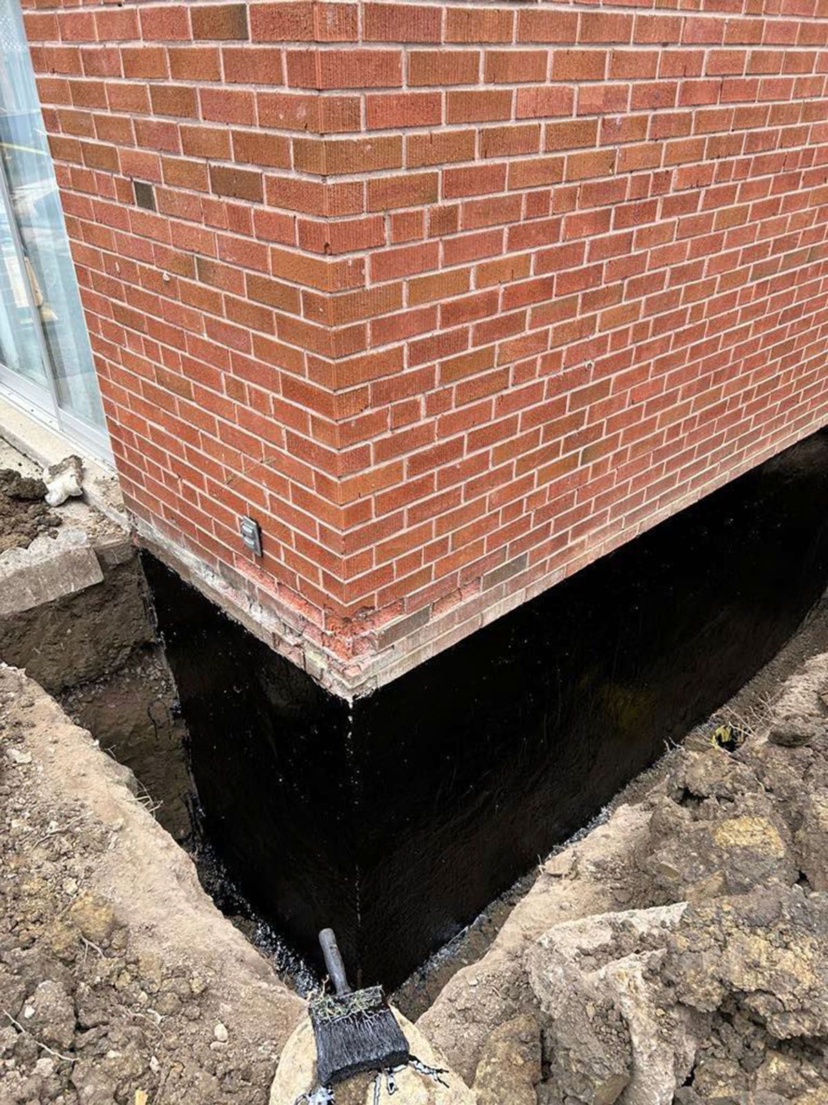 Red brick building corner with foundation waterproofing, in a freshly dug trench