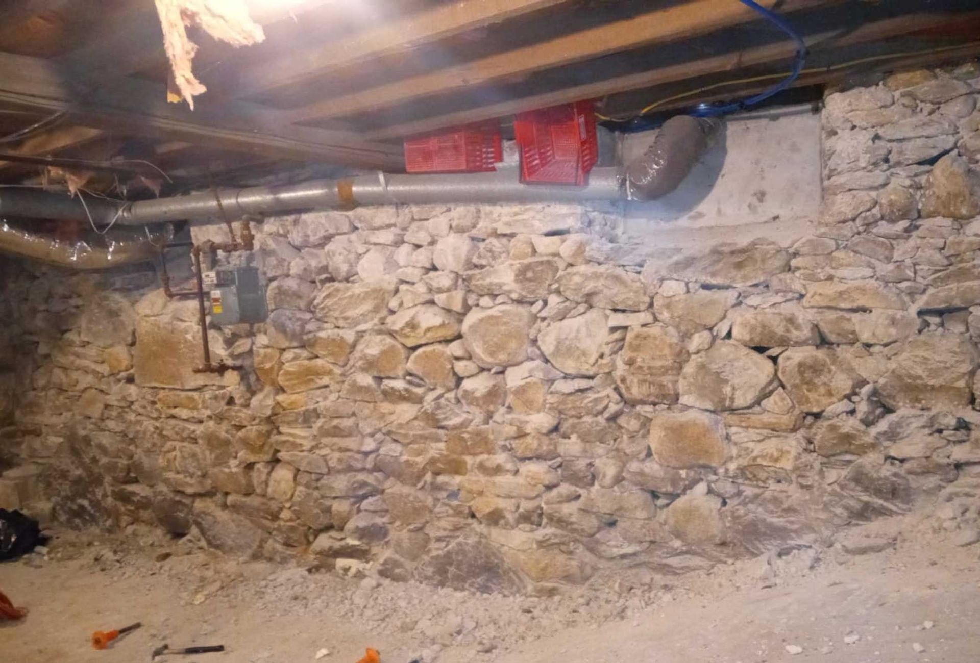 Stone foundation wall in a basement, with exposed pipes and ductwork.