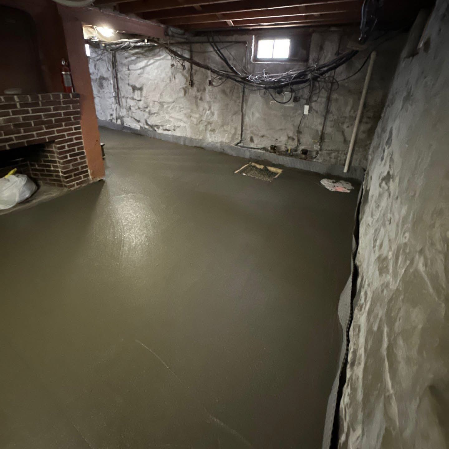 Basement with newly poured gray concrete floor; exposed brick fireplace and stone walls.