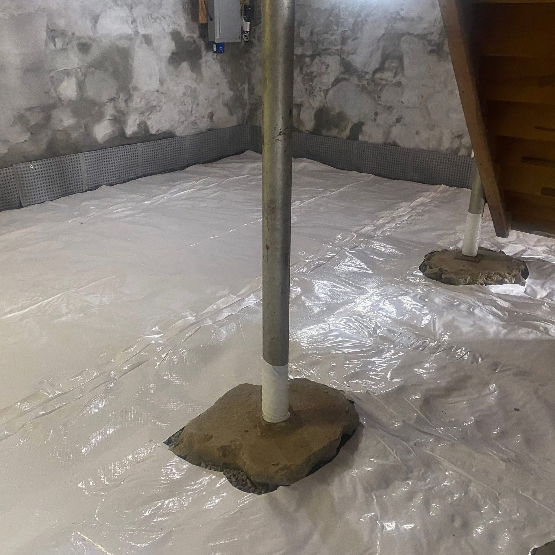 White vapor barrier covering a basement floor, a metal pole, and concrete support beams.