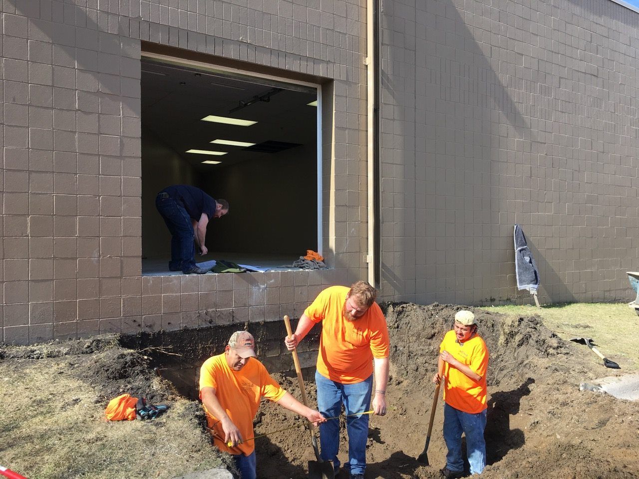 Three men are digging in the dirt in front of a building