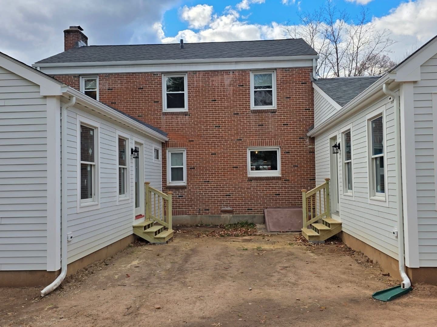 Back of a red brick building with two white-sided additions on each side. A gravel area is in front of the buildings.