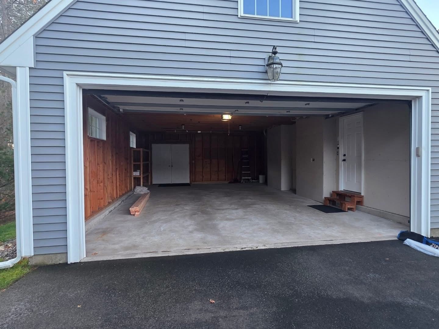 Open garage with gray siding, concrete floor, interior storage, and side door.