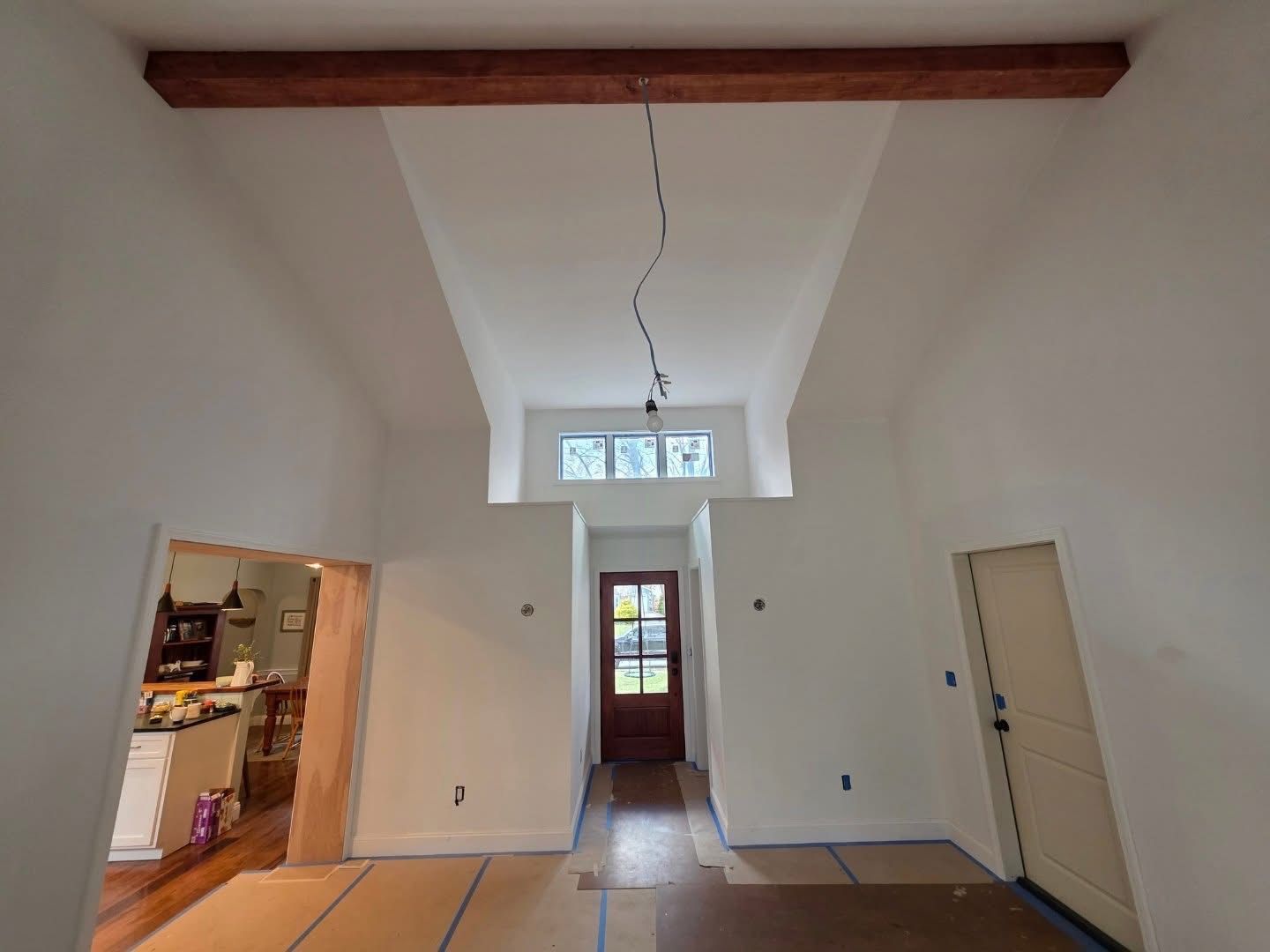 Interior view of a white-walled room with a tall ceiling, a wooden beam, and a doorway.