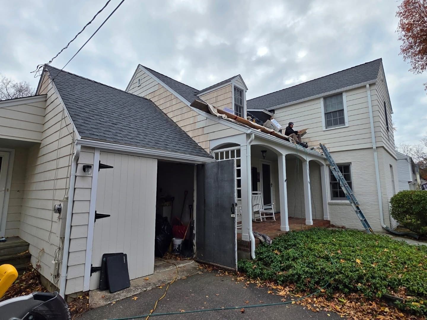 House with roof being repaired. Workers on roof, ladder against wall, cloudy day.
